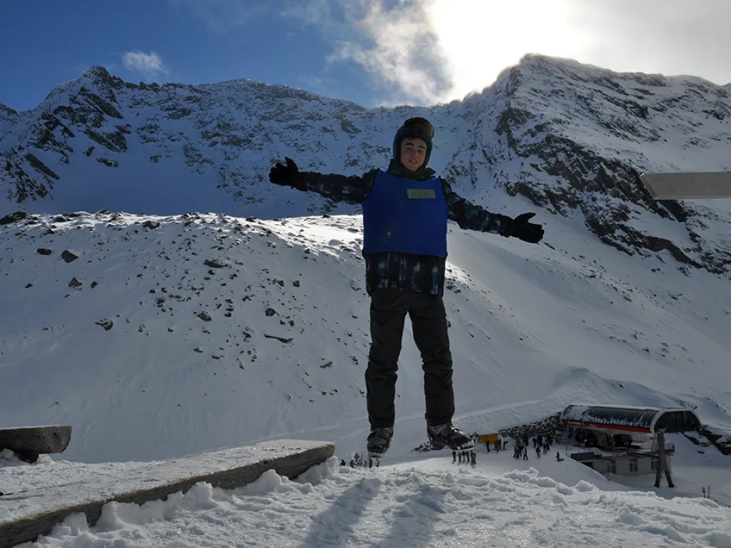 Person steht mit ausgebreiteten Armen vor der Bergkulisse.